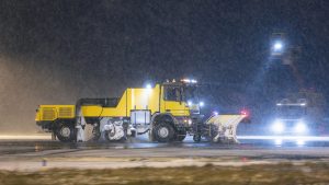 Snowplough convoy clearing airport runway with rubber blades to avoid damaging in-pavement lights