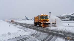 Airport snowplough convoy clearing runway with elevated edge lights visible along the sides
