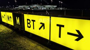 Direction taxiway sign with black text and arrows on yellow background showing the way to adjacent taxiways